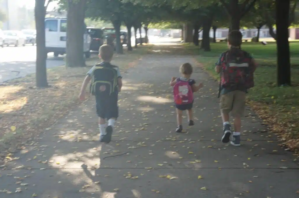 Three children walking down sidewalk with backpacks