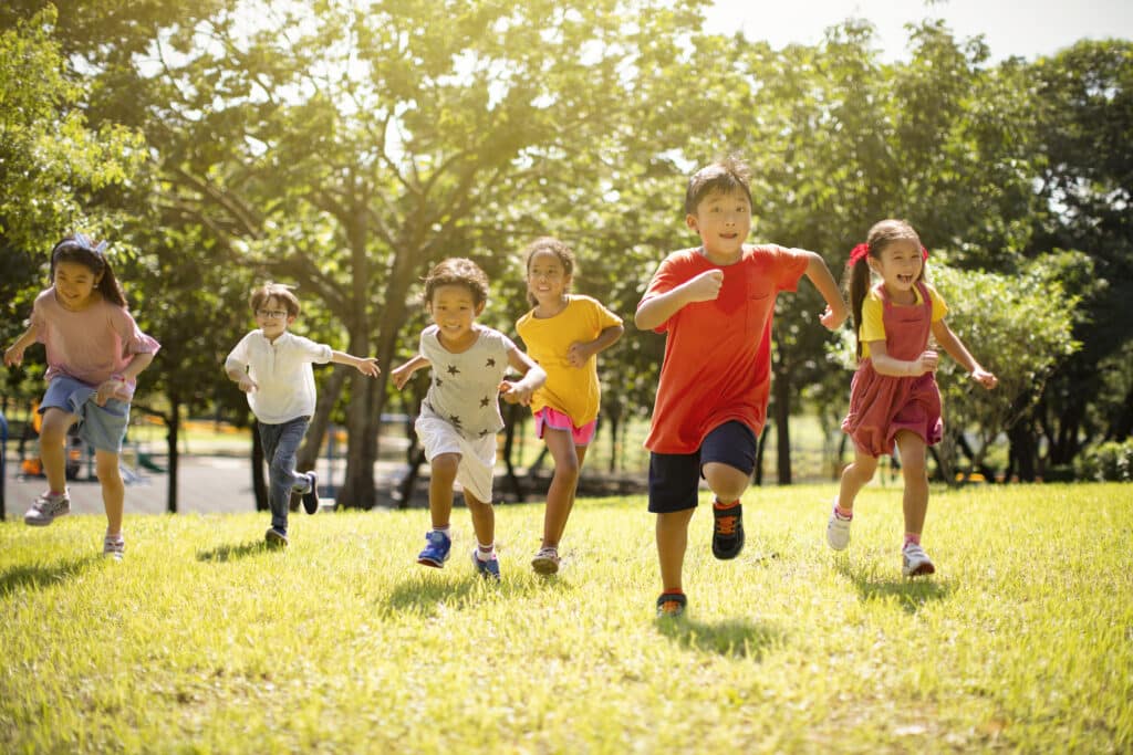 Group of multi-ethnic children smiling and racing across grassy area