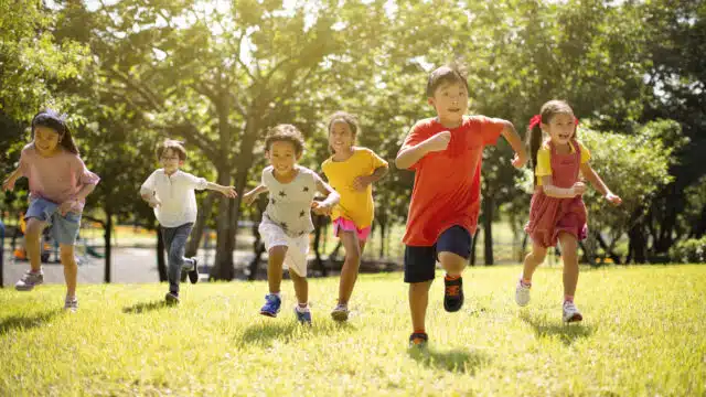 Group of multi-ethnic children smiling and racing across grassy area