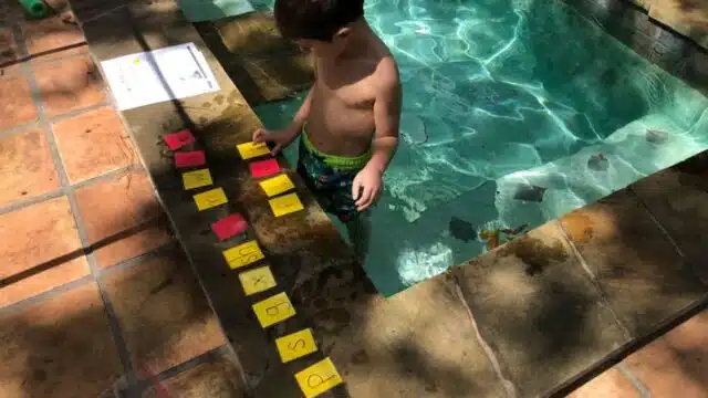 Child in a pool playing Switch It with yellow consonant cards and red vowel cards.