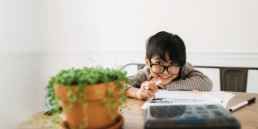 Child with glasses at table with marker in hand smiling.